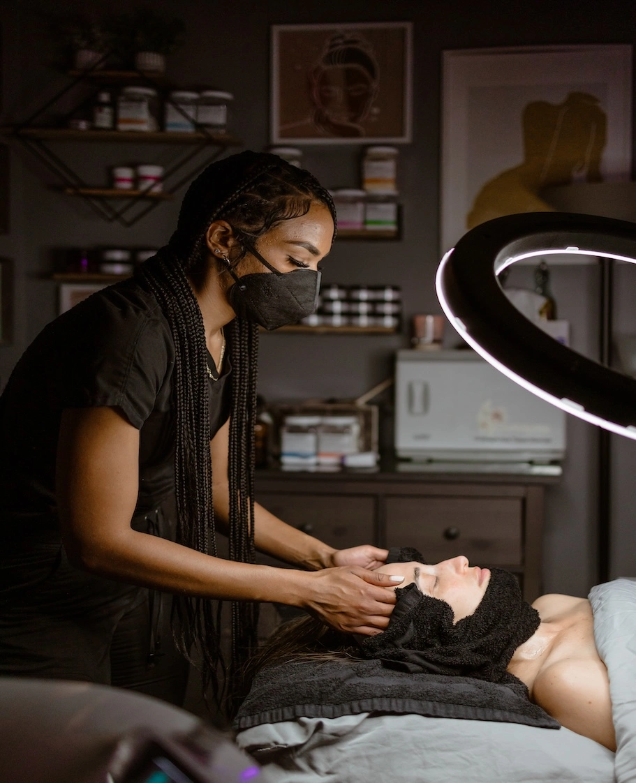 A beautician in a mask performs a skincare treatment on a client in a salon.